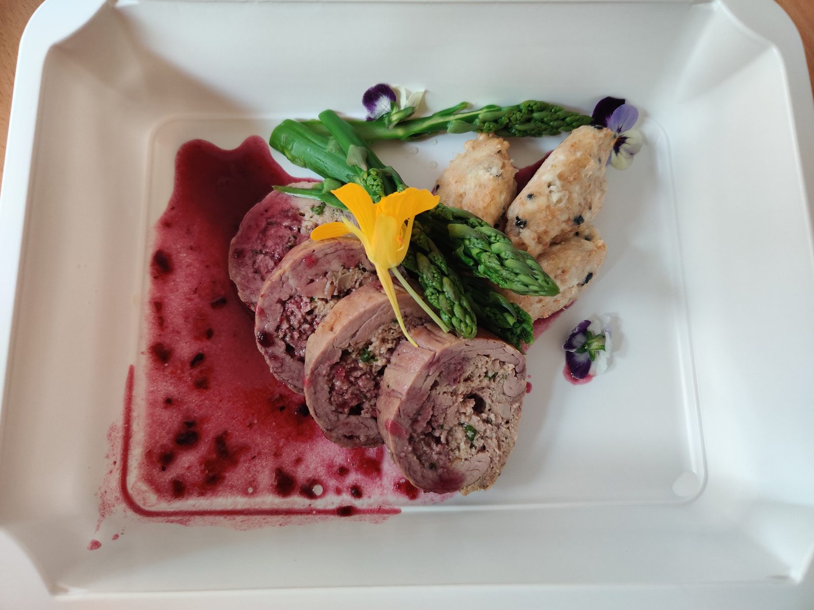 A plated meat roulade with asparagus and berry sauce