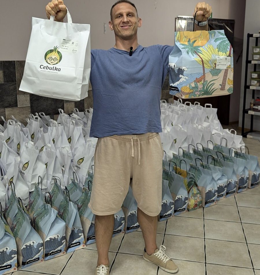 Paweł holding up two branded Cebulka delivery bags over rows of packed bags