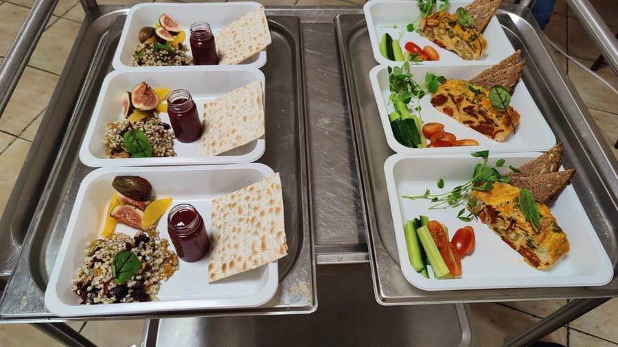 Six portioned meals on trays on a stainless-steel kitchen cart, ready for packing